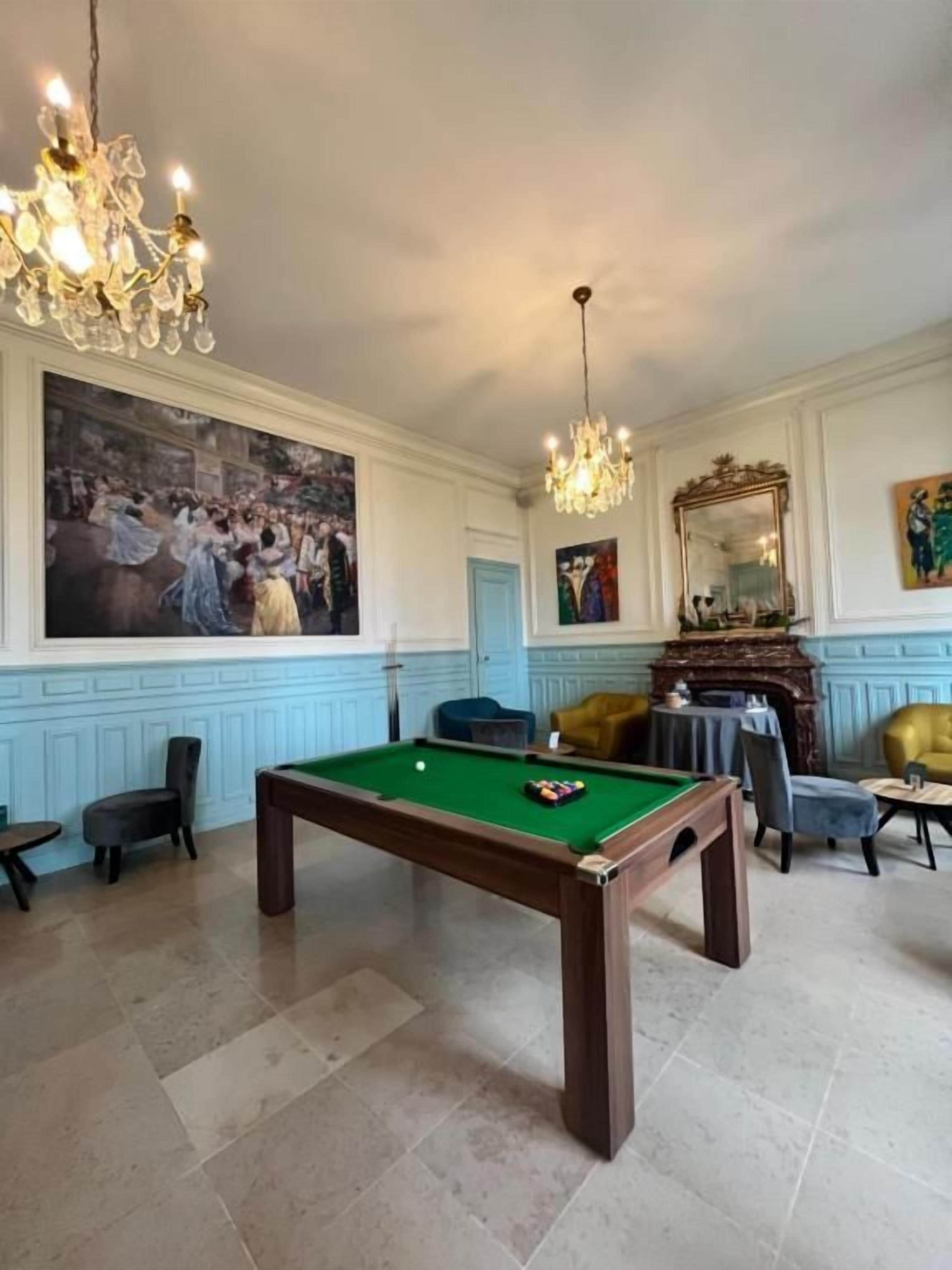 A billiards table in a room with a fireplace, a large painting, and a chandelier.