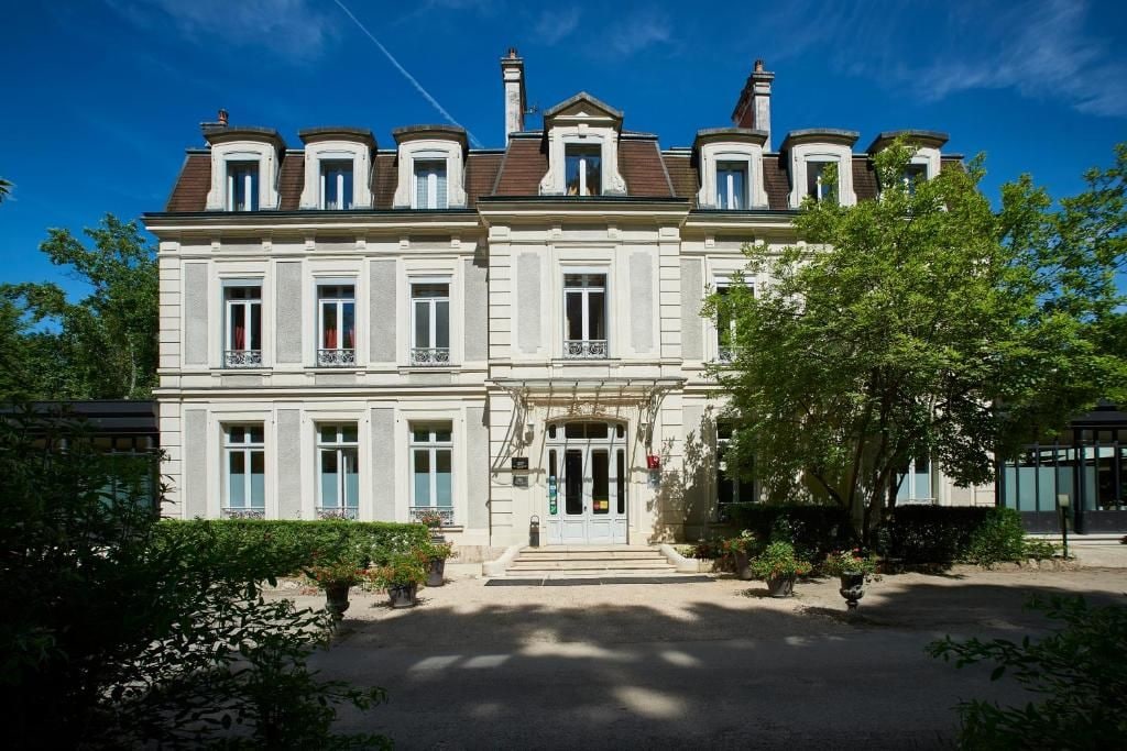 Ein zweistöckiges Gebäude mit einer symmetrischen Fassade, großen Fenstern und einem zentralen Eingang mit einer Treppe.