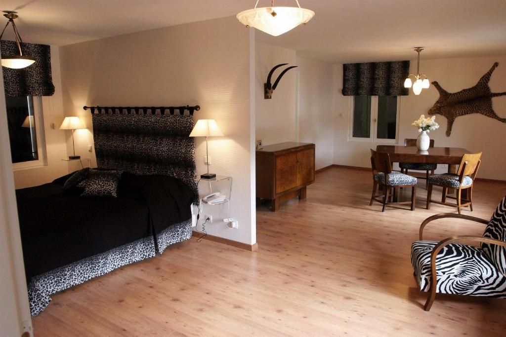 A room with a bed, a dining table with chairs, and a zebra-patterned chair.