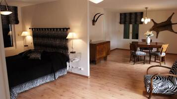 A room with a bed, a dining table with chairs, and a zebra-patterned chair.