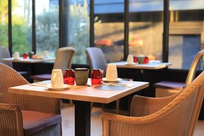 Comedor con mesas dispuestas para dos, sillas y vistas al exterior a través de grandes ventanales.