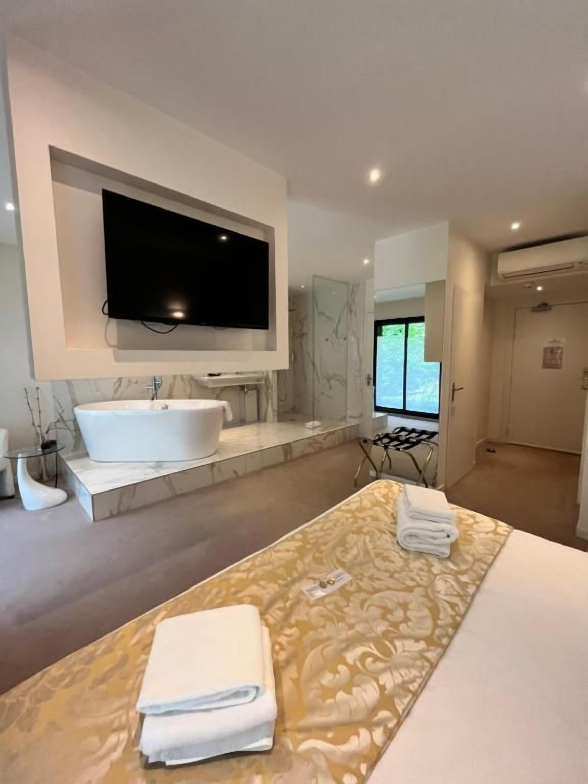 Habitación de hotel moderna con una cama grande, televisor montado, bañera y vistas al exterior.