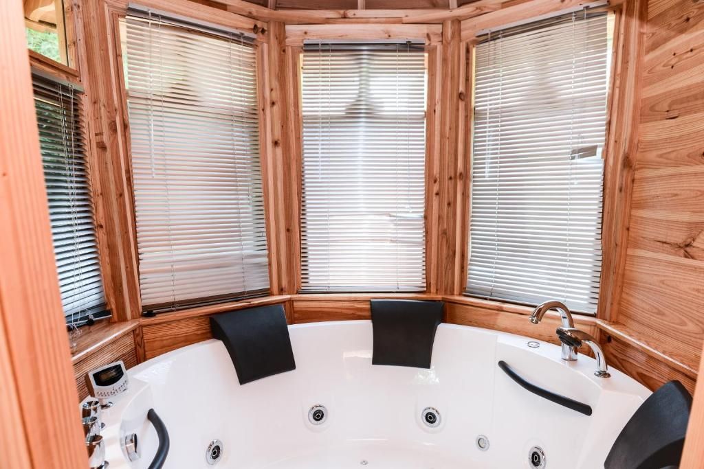 A wooden cabin with a large bathtub, wooden blinds, and a window seat.