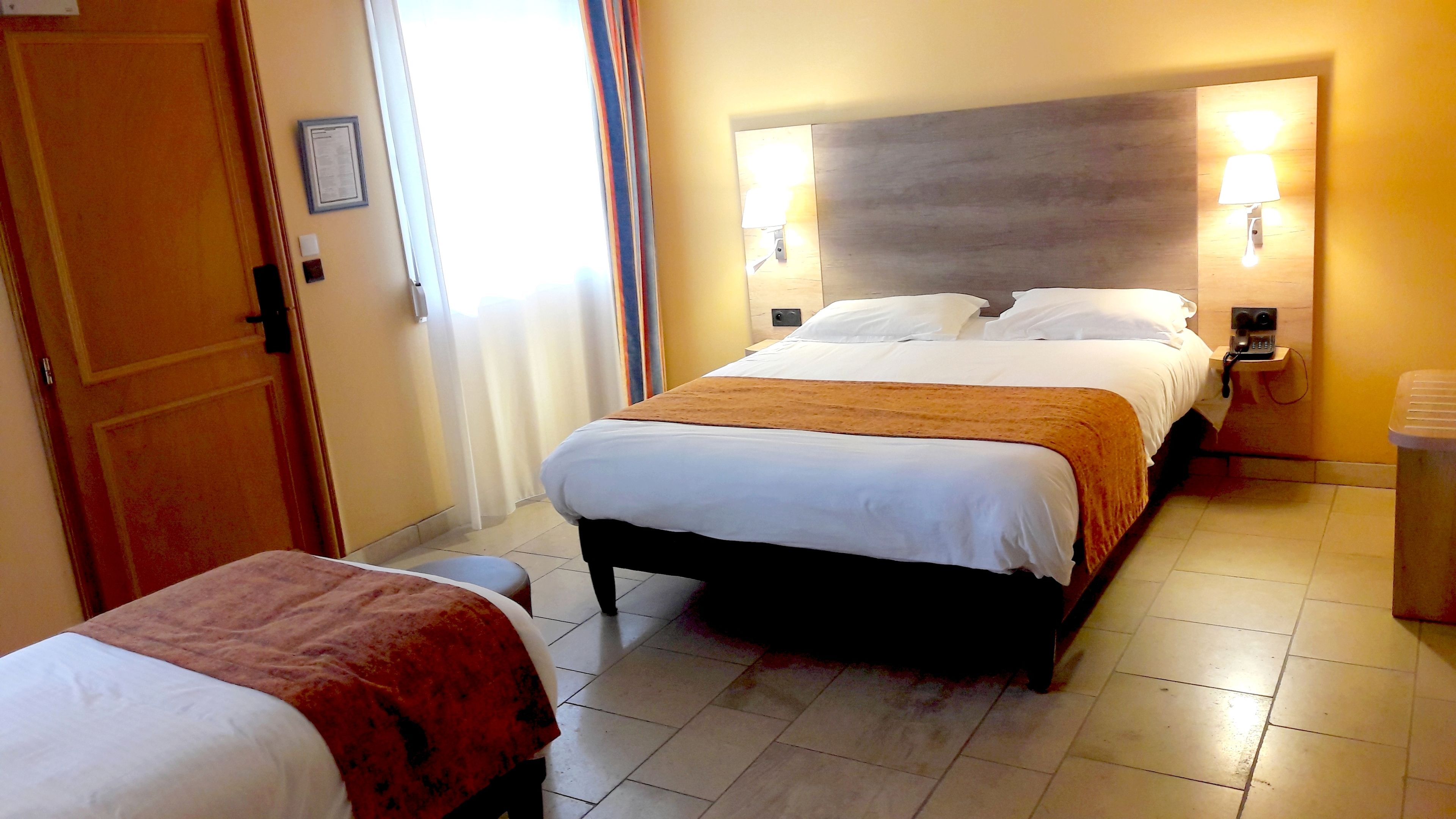 A hotel room with a bed, bedside tables, and a trash bin.