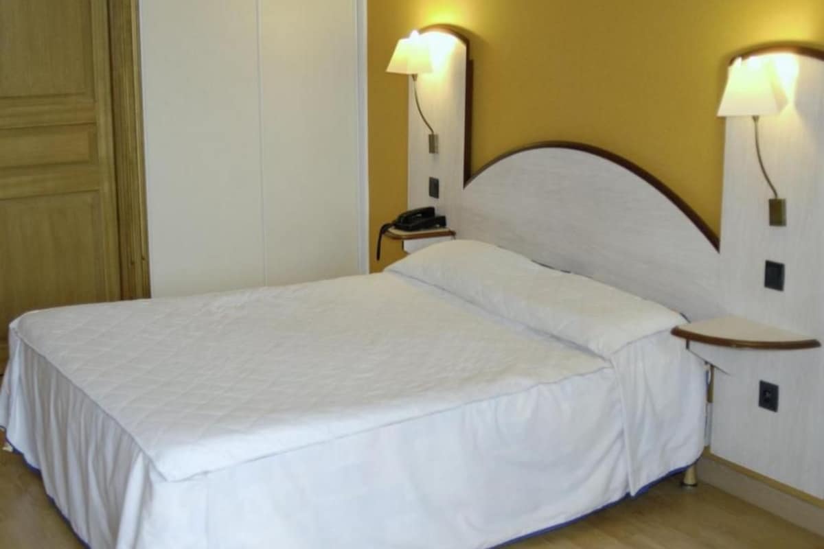 A neatly made bed with white linens in a room with wooden flooring and two bedside lamps.