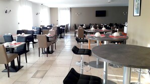 A spacious dining area with multiple tables and chairs, a flat-screen TV mounted on the wall, and a ceiling-mounted air conditioning unit. - Logis De France Des Sources (Creney-pres-Troyes)