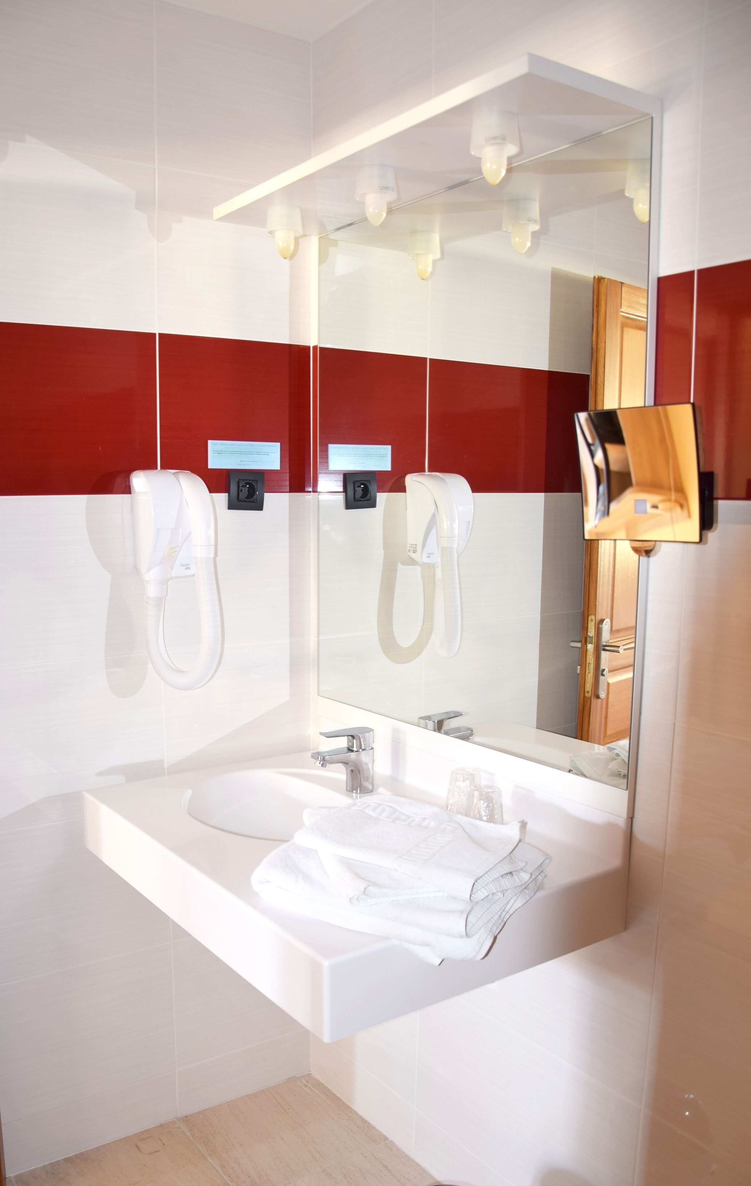 Un baño moderno con un espejo grande, dos secadores de manos blancos, un lavabo y un perchero para toallas.