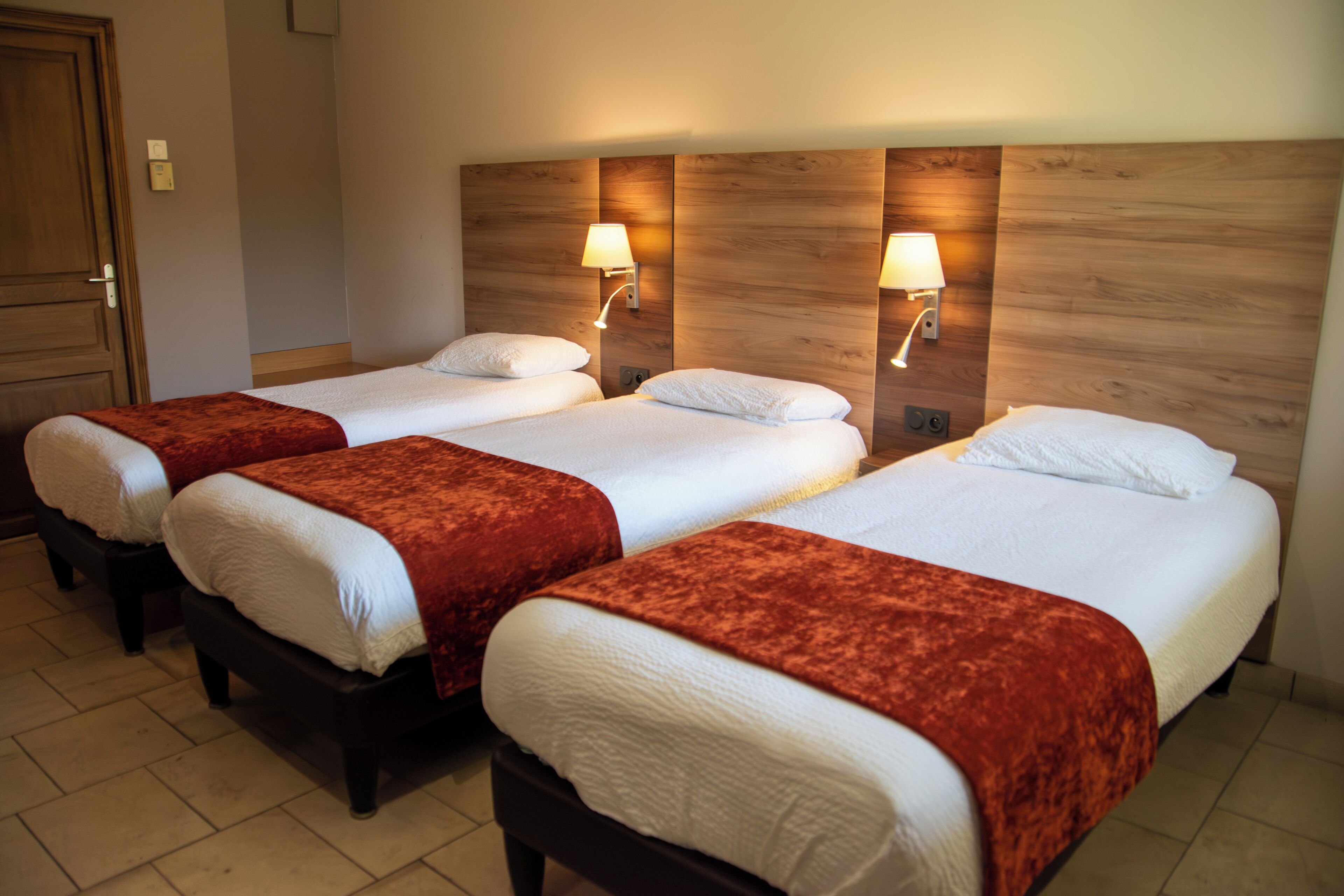 A hotel room with three single beds, each with a red throw blanket and white bedding.