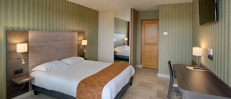 Une chambre d’hôtel avec un grand lit, des lampes de chevet, un bureau et un téléviseur fixé au mur.