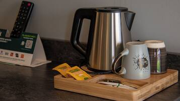 A tray with a stainless steel kettle, a white mug with a design, and two small containers, likely for condiments, on a wooden tray.