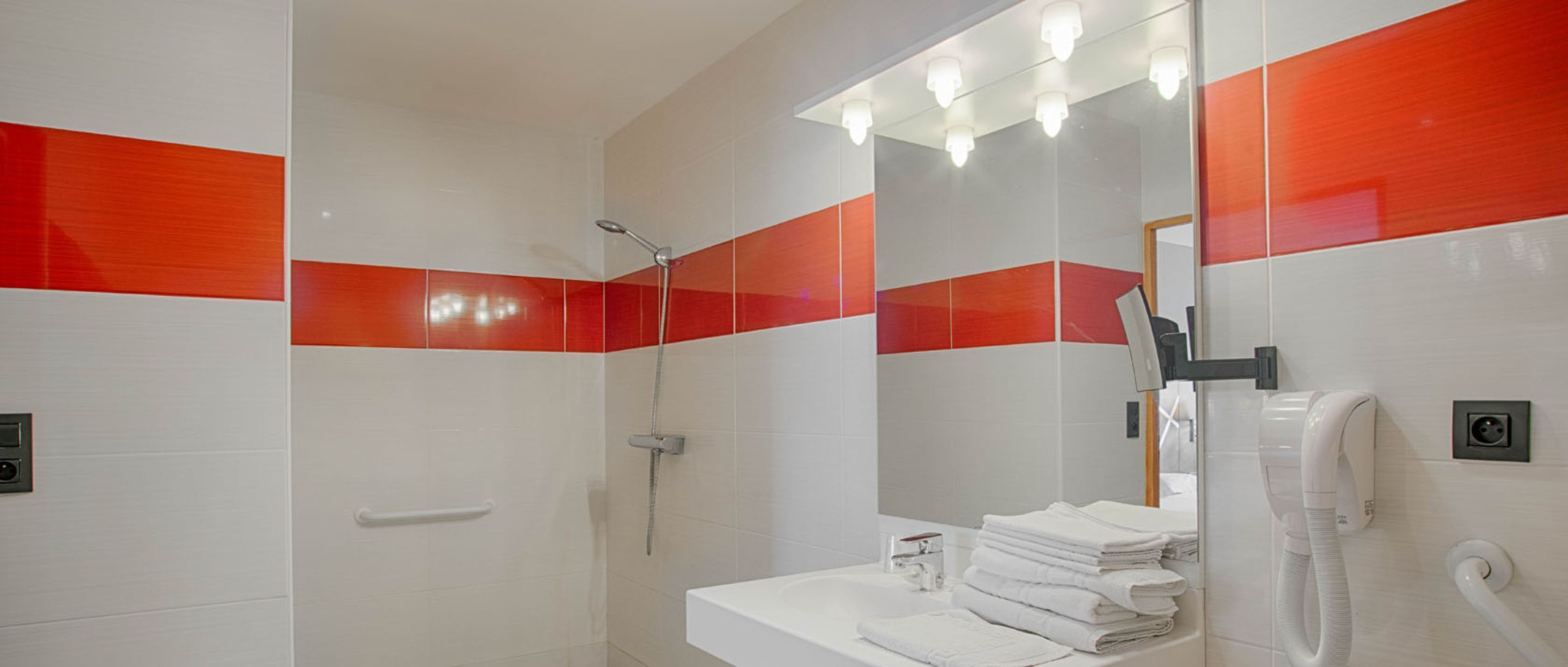 Une salle de bain avec une douche, un lavabo avec des serviettes pliées et un miroir avec éclairage.
