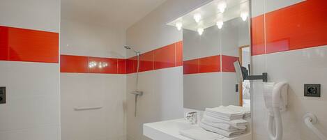 Une salle de bain avec une douche, un lavabo avec des serviettes pliées et un miroir avec éclairage.