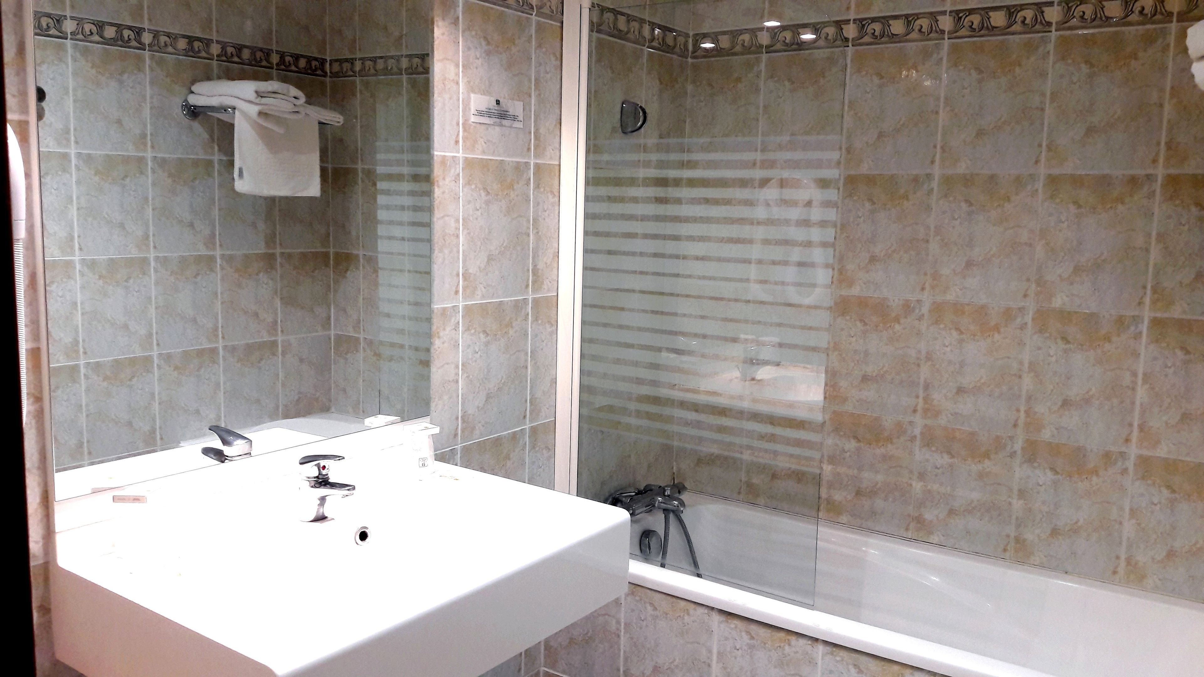 A bathroom with a white sink, a mirror, a towel rack, and a shower area with a glass door.