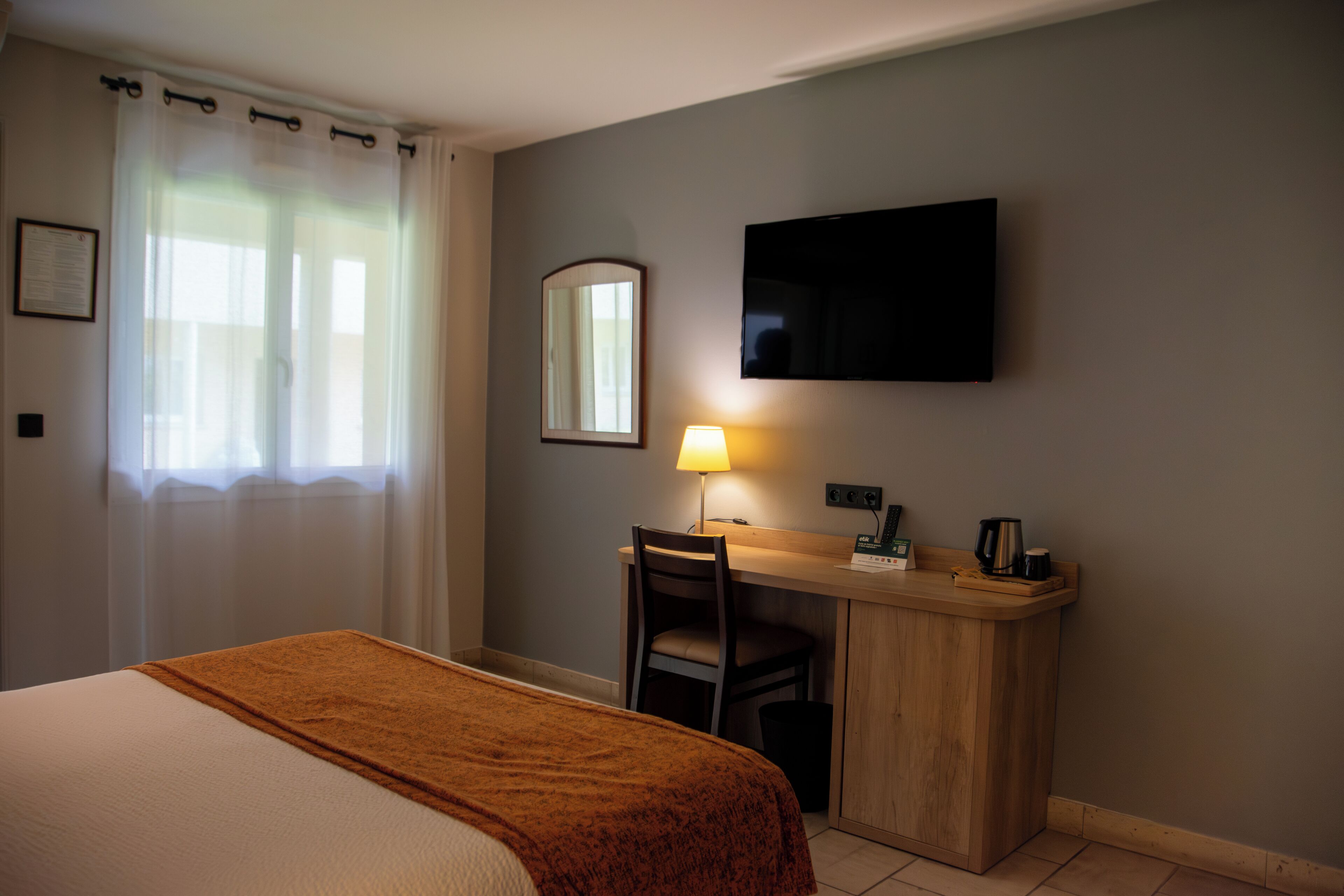 Habitación de hotel con cama, escritorio, silla, televisor y lámpara.
