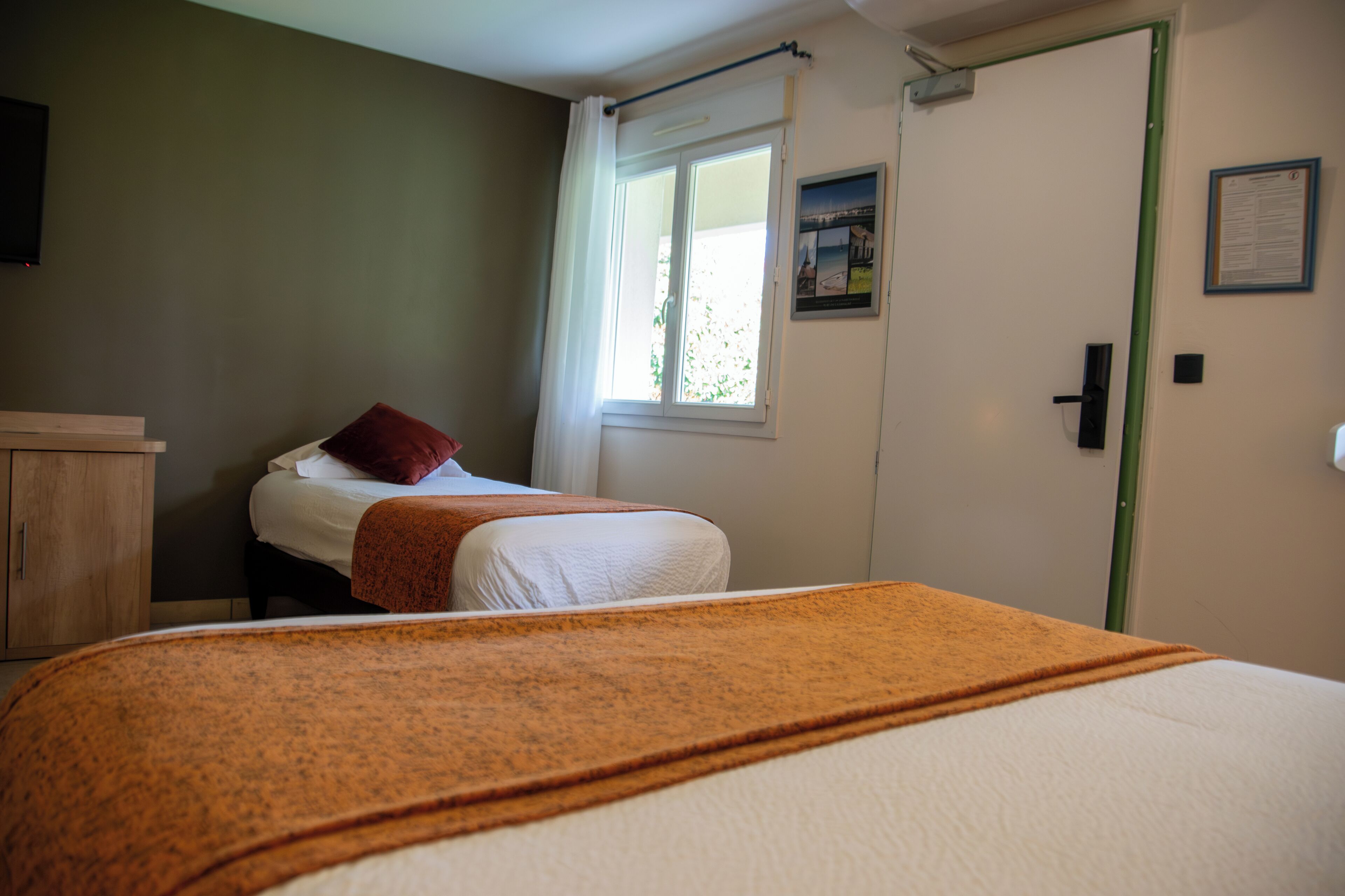 A bedroom with a bed, a window with curtains, a door, and a wall-mounted picture.