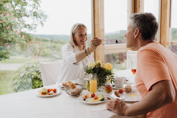 A breakfast setting with a table set for two, featuring a variety of fruits, pastries, and a glass of orange juice. - Das Eisenberg (Sankt Martin an der Raab)