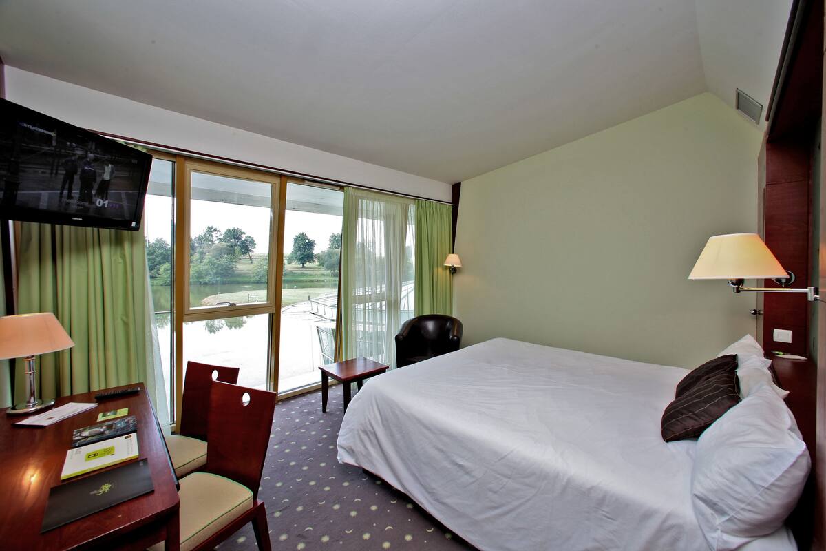 Une chambre d’hôtel avec un lit, un bureau doté d’une lampe, une chaise et un téléviseur fixé au mur.