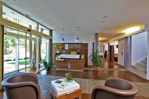 Un vestíbulo espacioso con una recepción, suelo de madera y amplias ventanas con vistas al exterior.