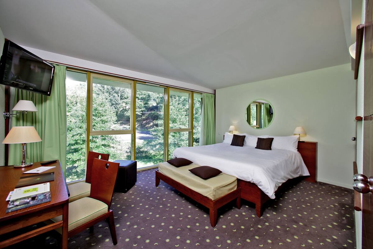 Une chambre d’hôtel avec un grand lit, un bureau avec une lampe, une chaise et un téléviseur fixé au mur.