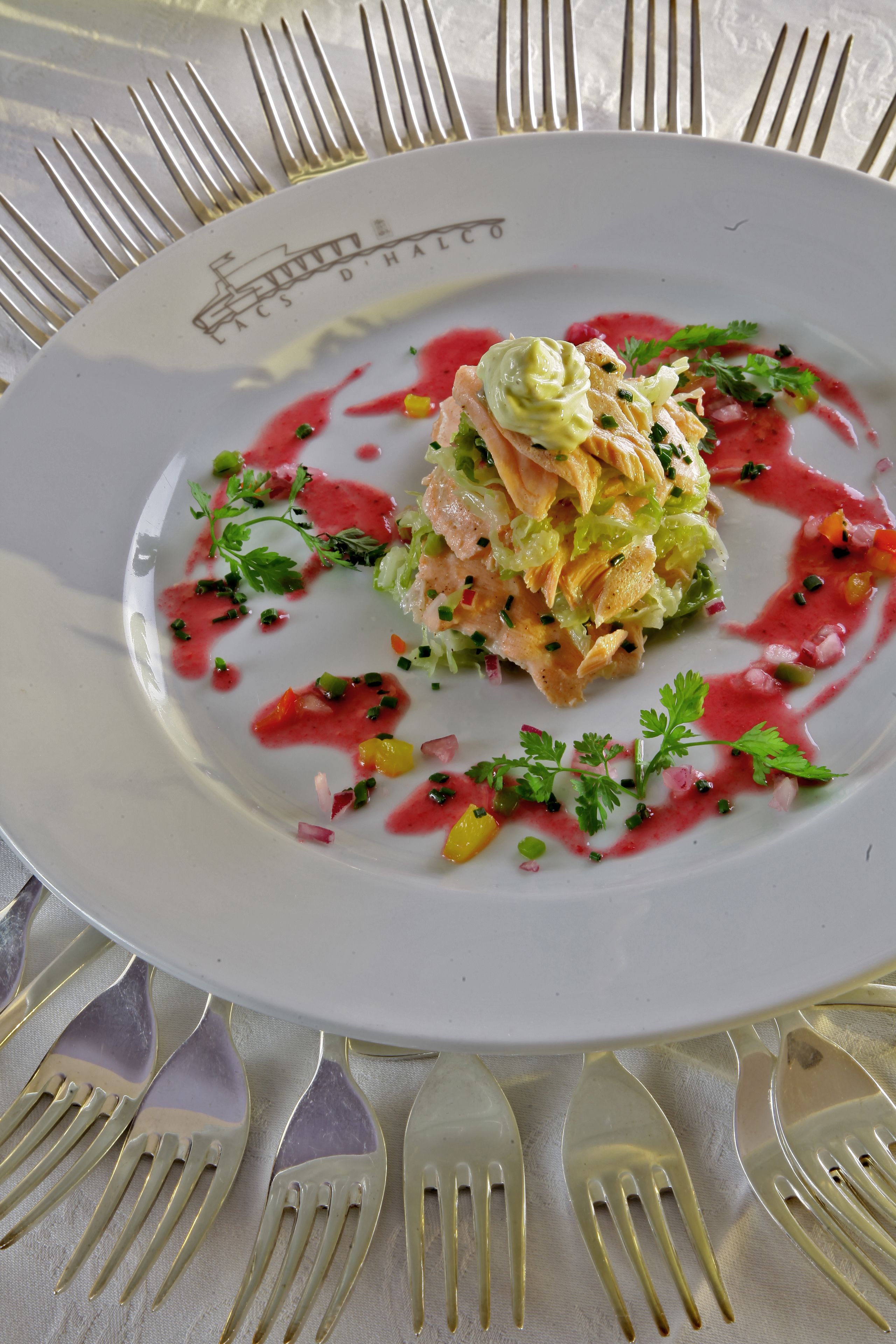 A white plate with a salad and sauce, surrounded by gold forks.