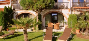 A courtyard with outdoor seating, a palm tree, and a building with a balcony. - Hazienda Apartmenthotel (Gernsbach)