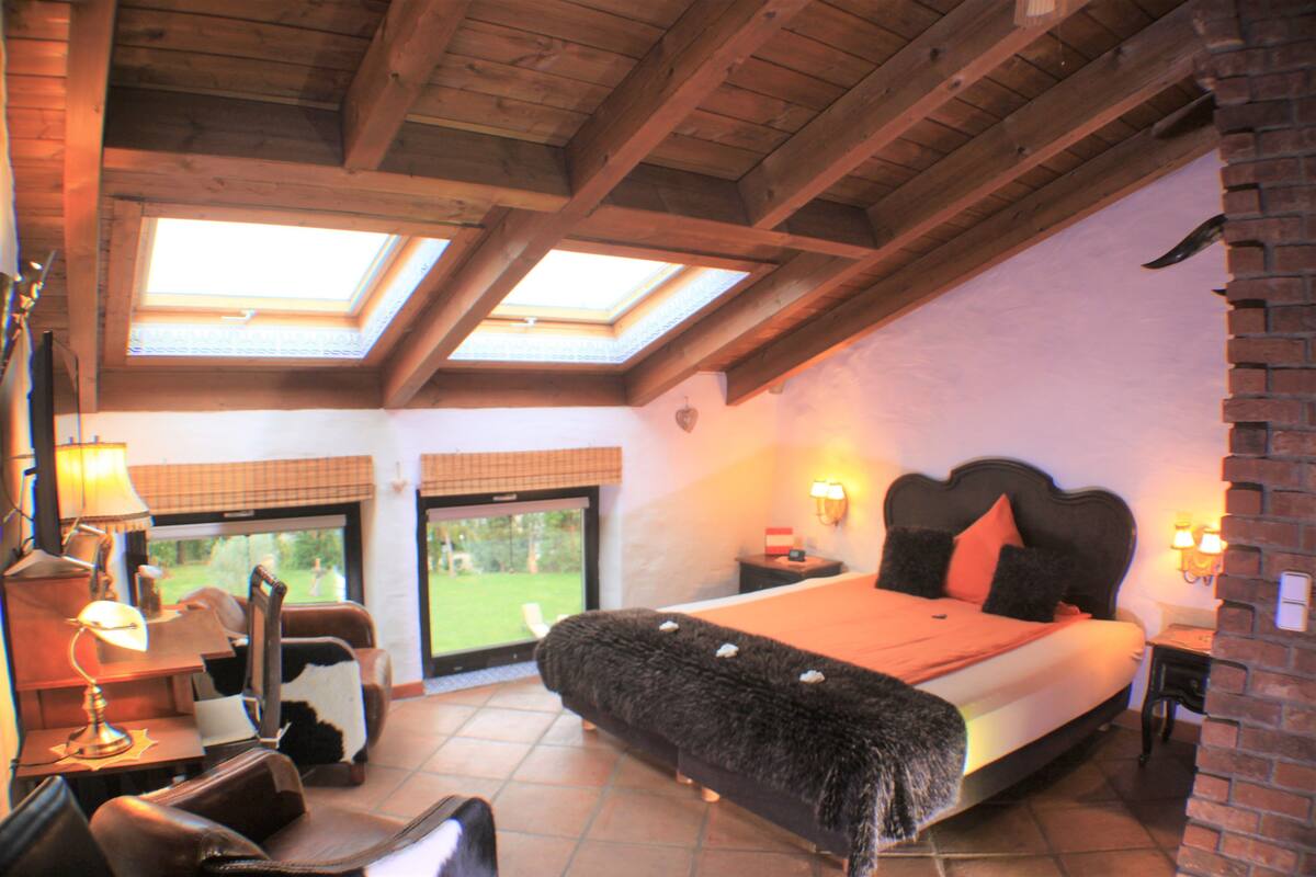 Une chambre avec un grand lit, des fenêtres de toit, un bureau avec une lampe et une vue sur l’extérieur.