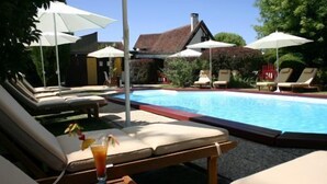 A poolside area with lounge chairs and umbrellas, a wooden table with a drink, and a house in the background. - Domaine de l'Arbrelle (Amboise)