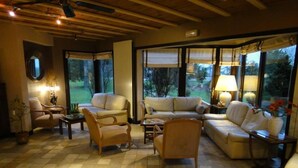 A spacious living room with a checkered floor, large windows offering a view of the outdoors, and a variety of seating options including a sofa, armchairs, and a coffee table. - Domaine de l'Arbrelle (Amboise)