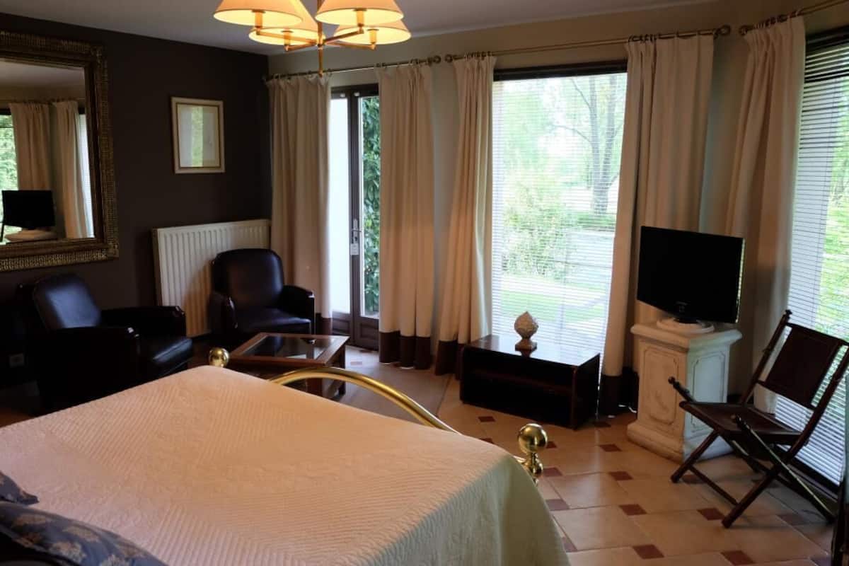 A hotel room with a bed, two chairs, a TV, and a window with curtains.