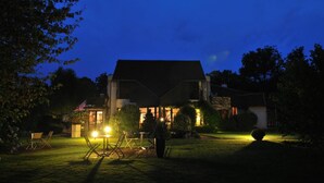 A house at night with a well-lit front yard, including a lawn and a small garden area.