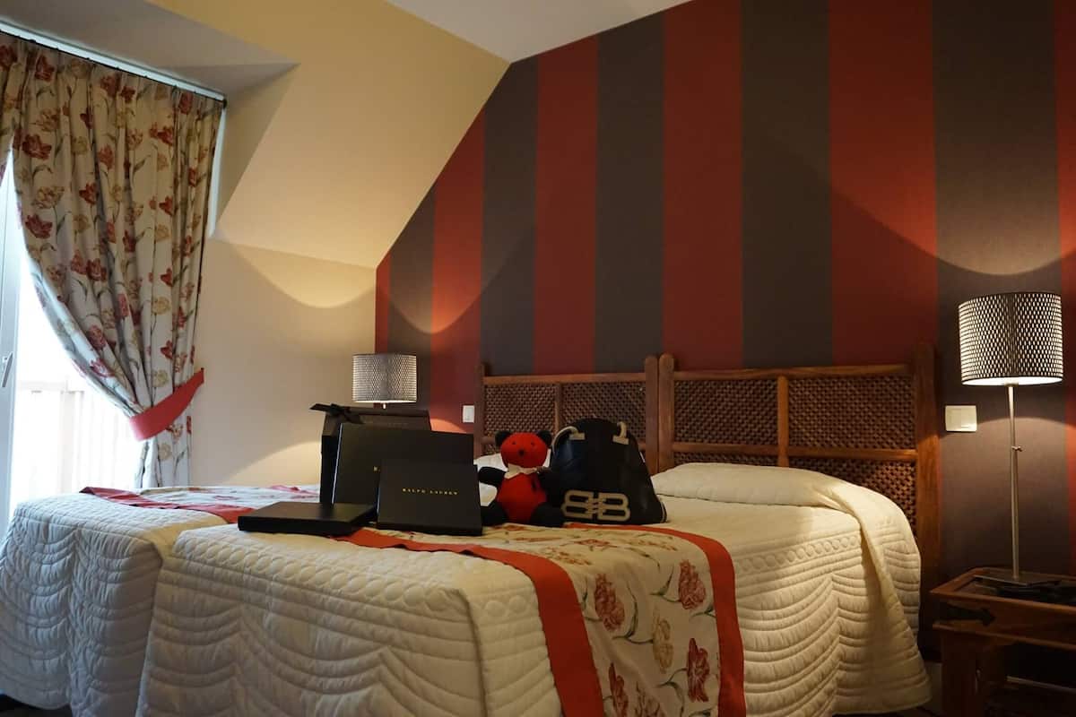 A hotel room with two beds, a laptop, a teddy bear, and a bag on one bed.