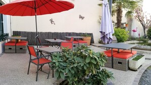 Un patio al aire libre con mesas y sillas, un paraguas rojo y un pequeño estanque con plantas.