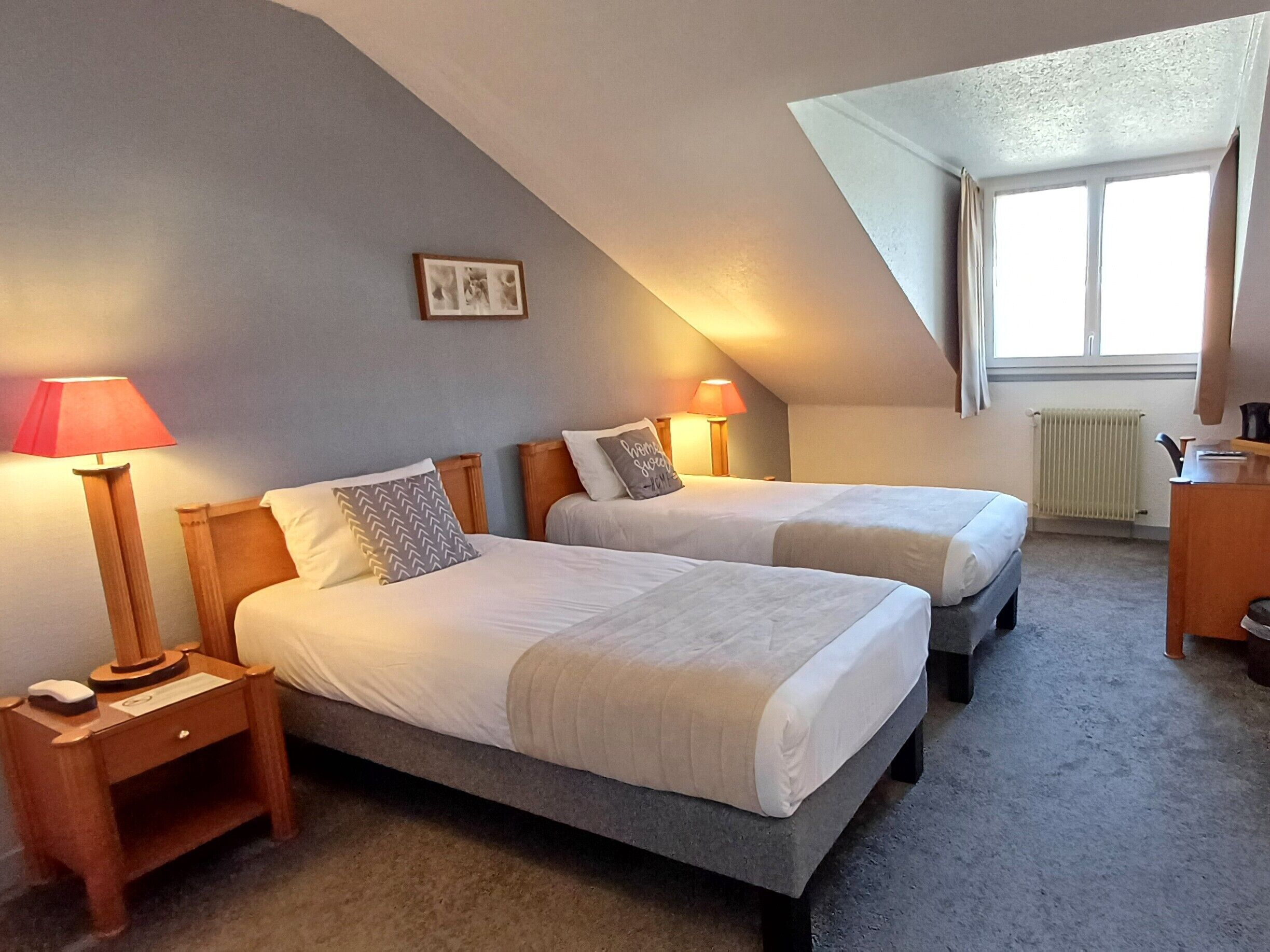 A room with two beds, each with a nightstand, lamps, and a picture on the wall.