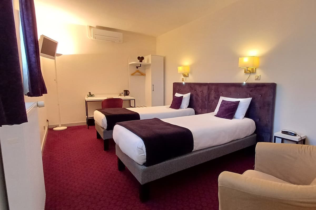 A hotel room with two beds, a desk, a chair, and a TV.
