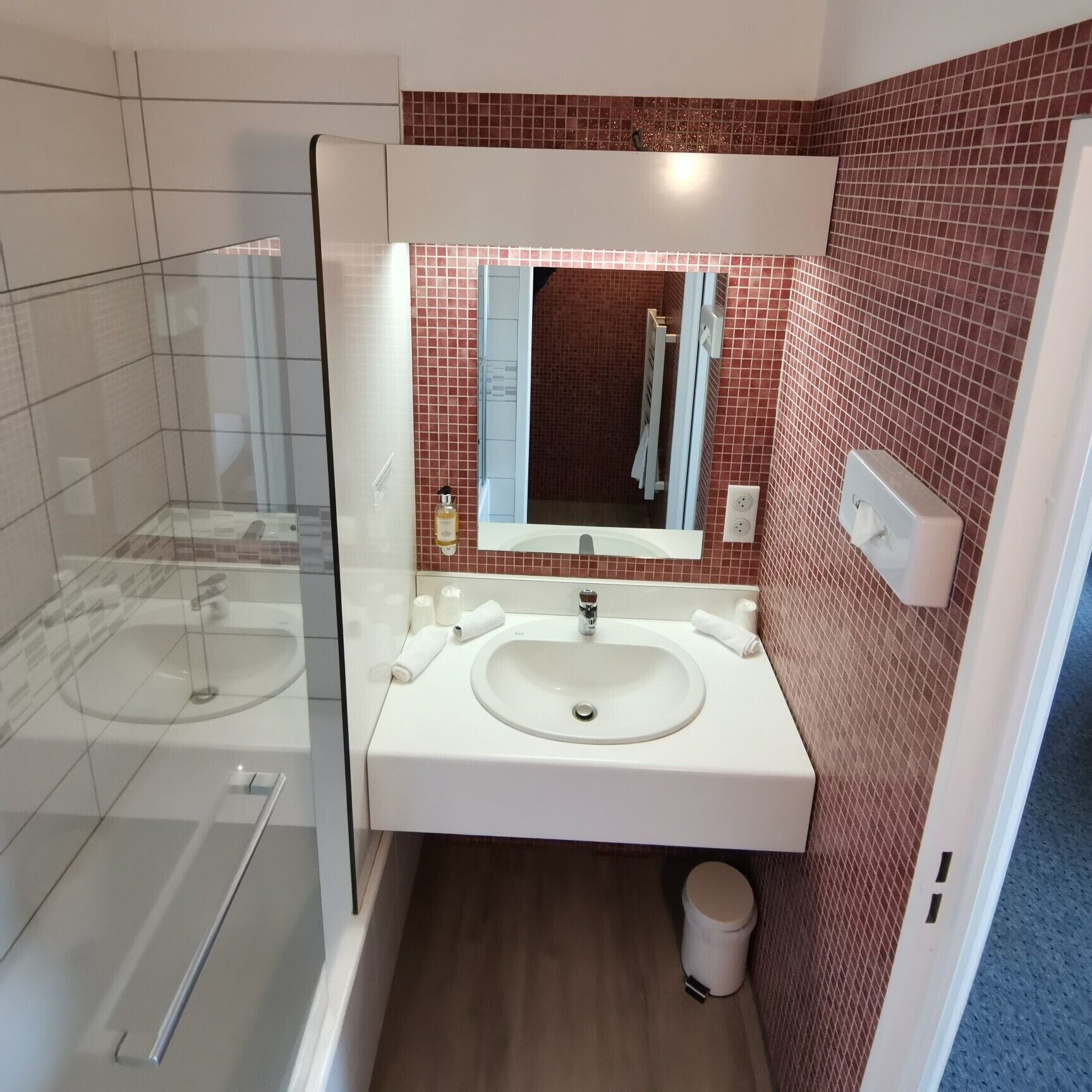 Un baño moderno con cabina de ducha de vidrio, un lavamanos blanco con un espejo encima y paredes con azulejos rojos.