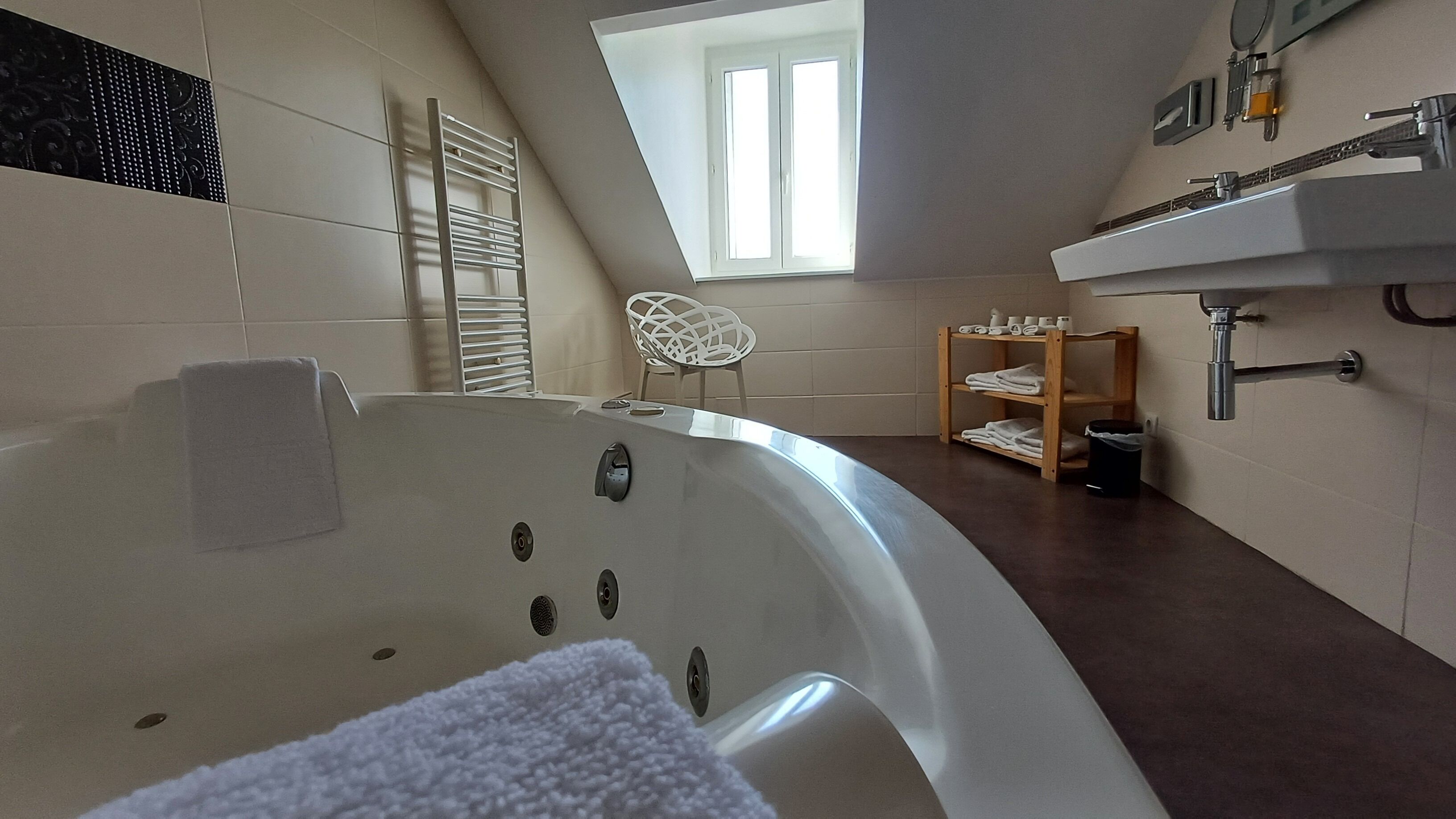 A modern bathroom with a freestanding bathtub, a towel rack, a wooden shelf with towels, and a skylight.