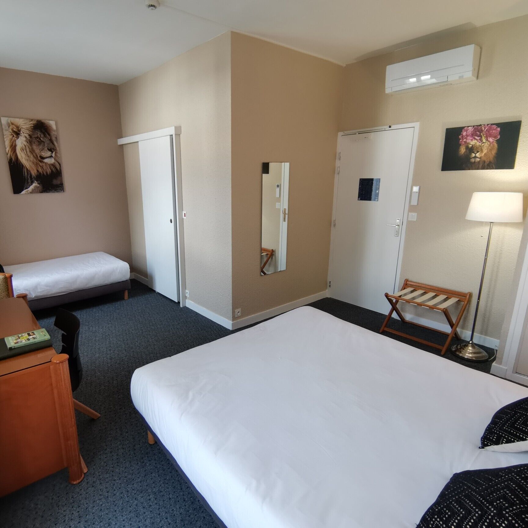 Et hotelværelse med to senge, et skrivebord, en stol, en gulvlampe og et spejl.
