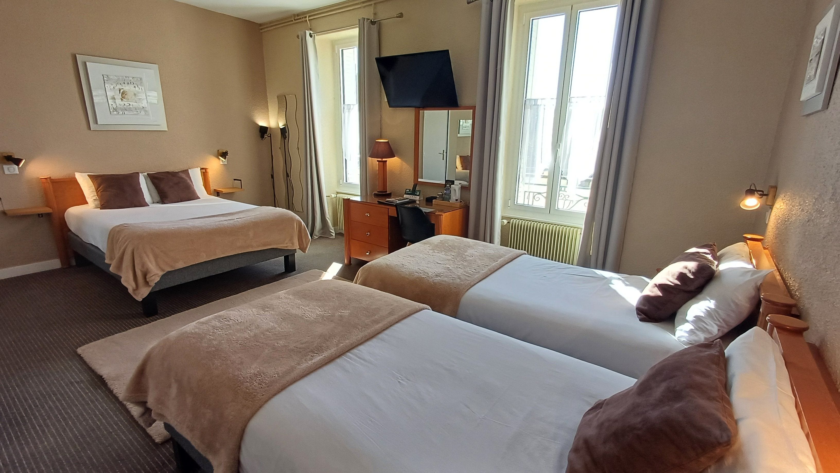 A hotel room with two beds, a desk, a TV, and a window with curtains.