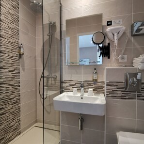 A modern bathroom with a glass-enclosed shower, a white sink with three faucets, a hairdryer, and a mirror. - Hôtel Le Cerf (Briare)