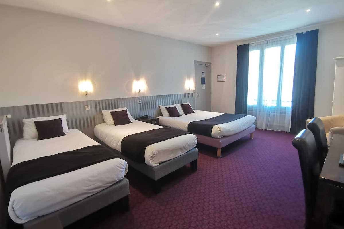 A hotel room with three beds, a desk, and a chair.