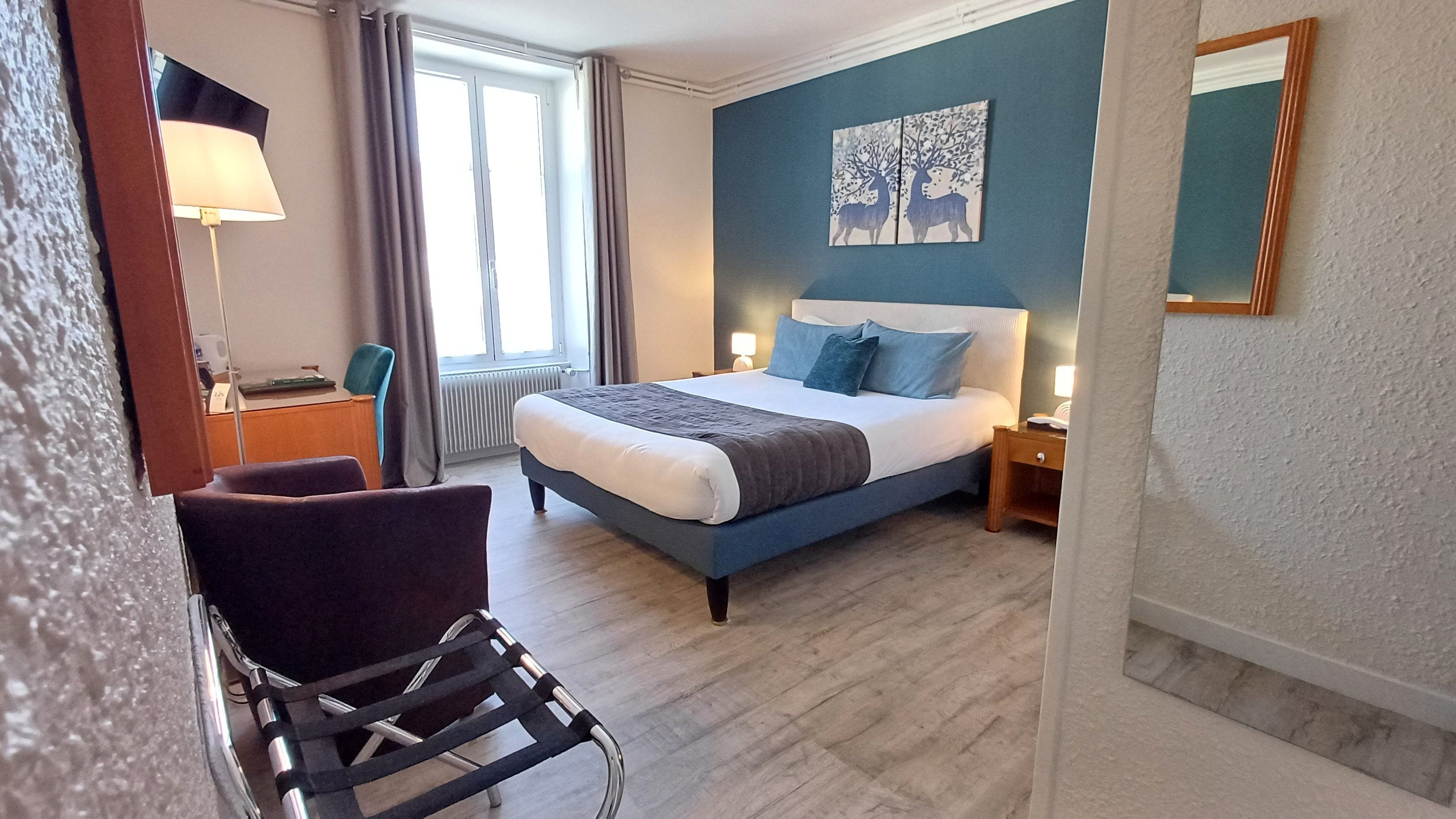Une chambre d’hôtel avec un lit, un bureau, une chaise et une fenêtre avec des rideaux.