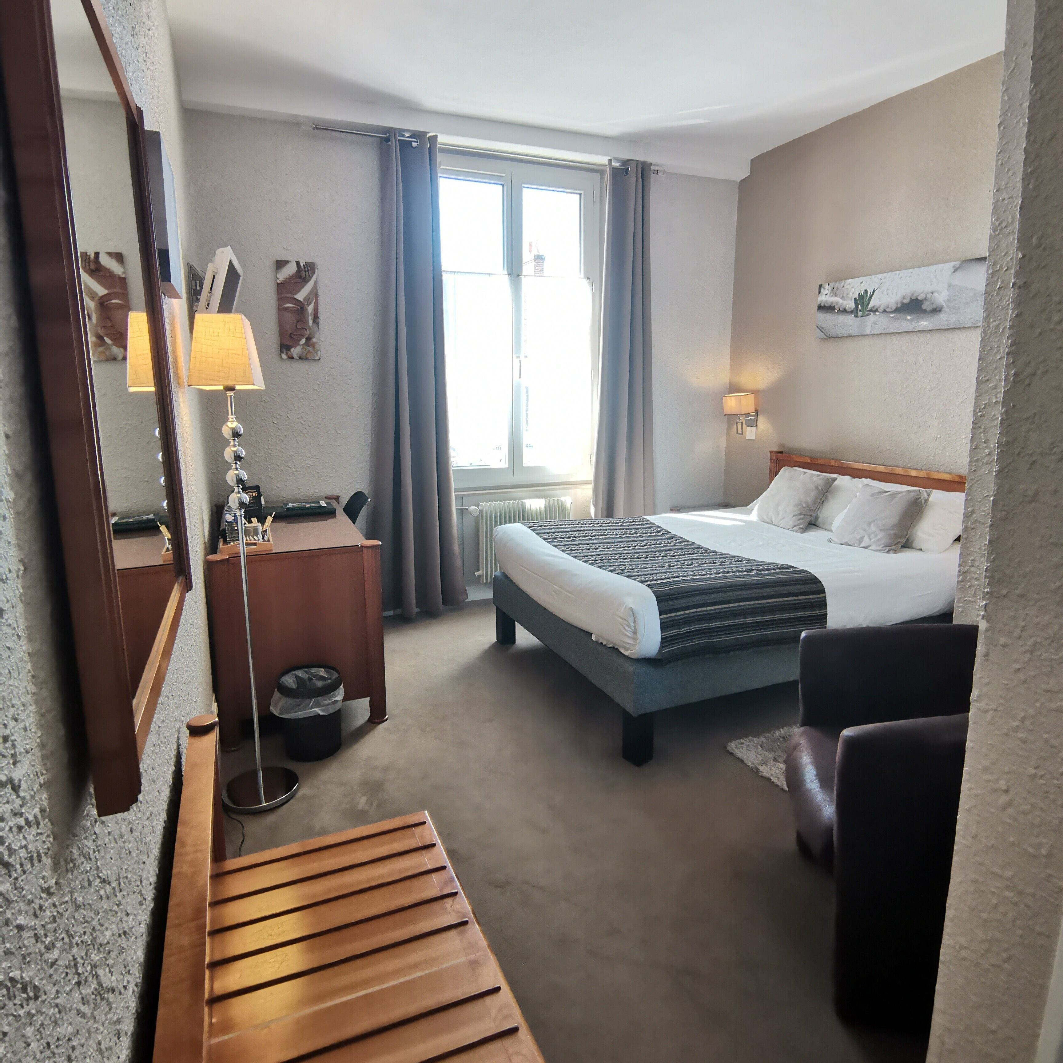 Une chambre d’hôtel avec un lit, une table de chevet, une lampe et une grande fenêtre avec des rideaux.