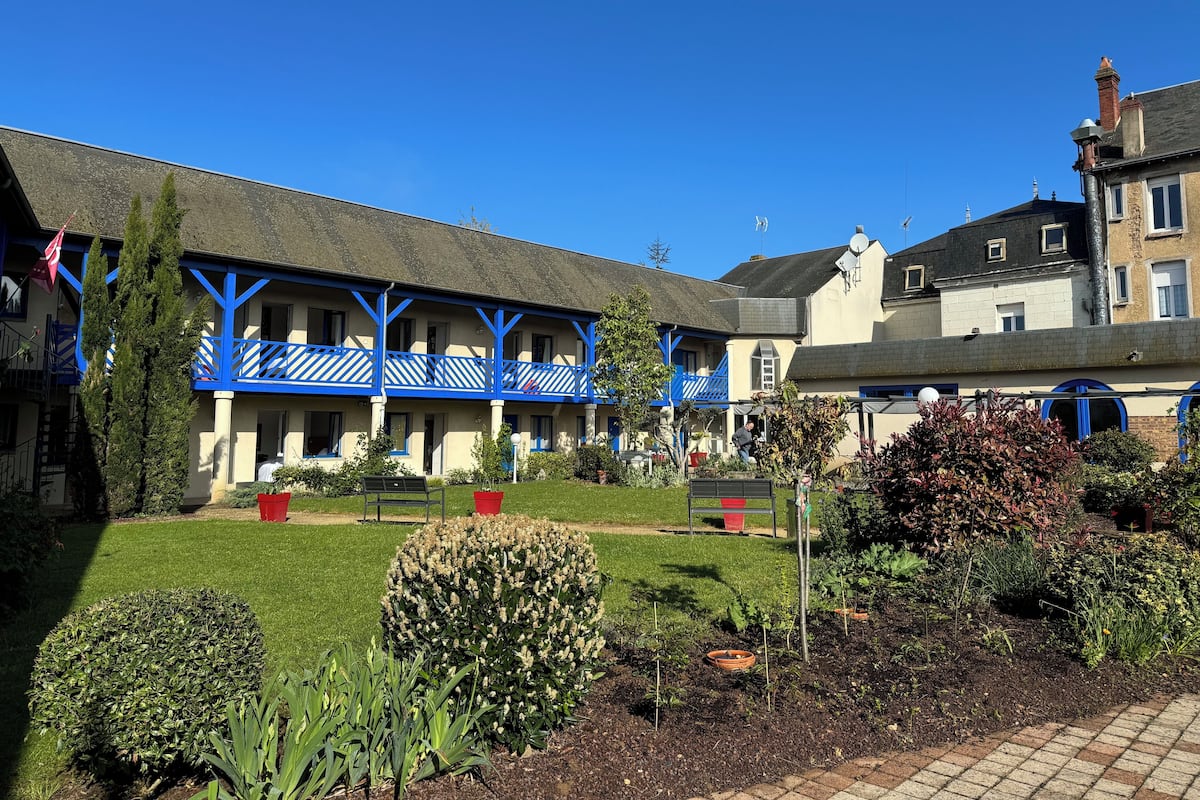 A courtyard with a building featuring blue balconies, a well-maintained lawn, and various plants.
