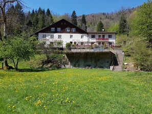 Un hotel con fachada blanca, un balcón y un puente de piedra que conduce a la entrada.