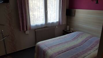 A bedroom with a bed, a radiator, a nightstand, a lamp, and a wall-mounted TV.