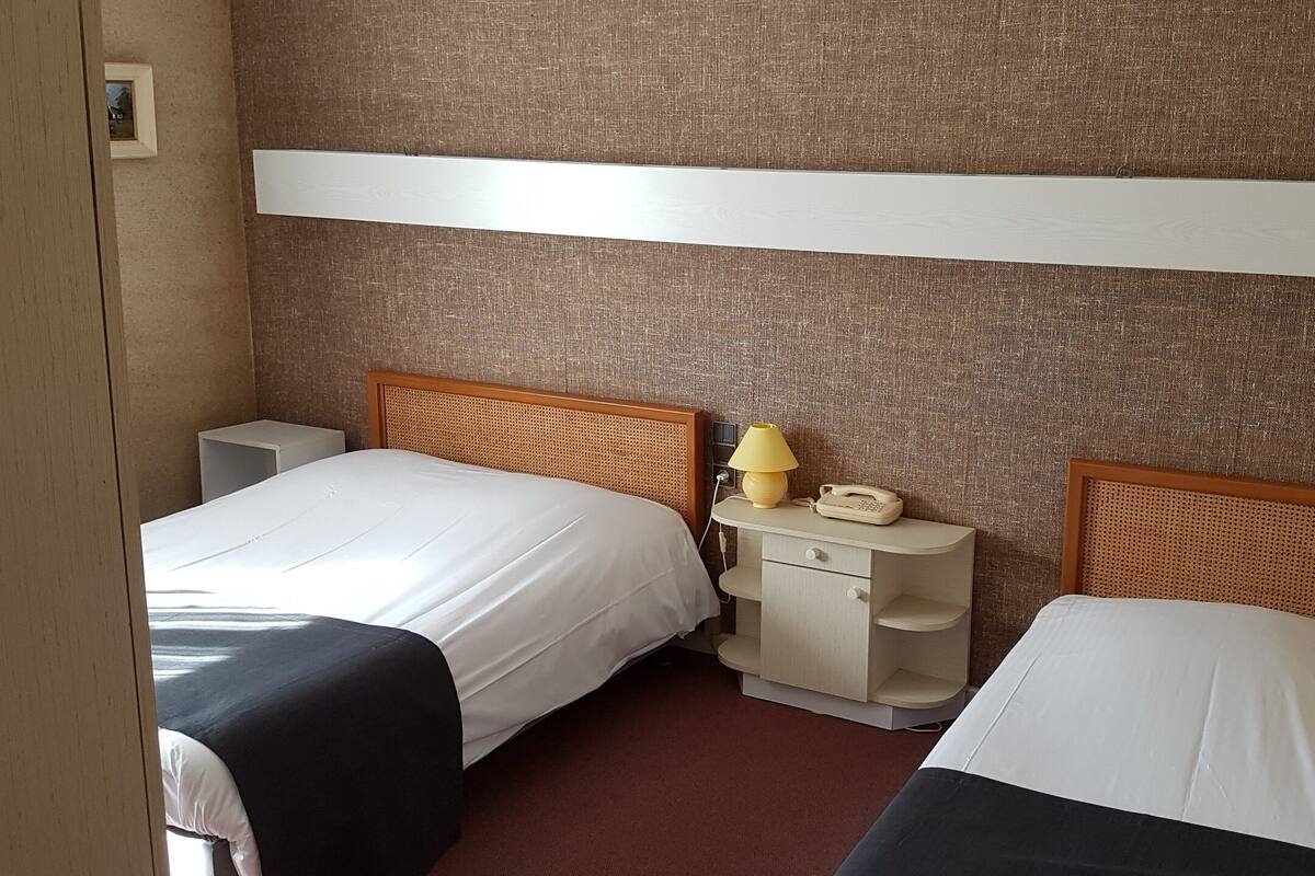 Ein Hotelzimmer mit zwei Einzelbetten, einem Nachttisch mit Lampe und Telefon sowie einem an der Wand befestigten Regal.