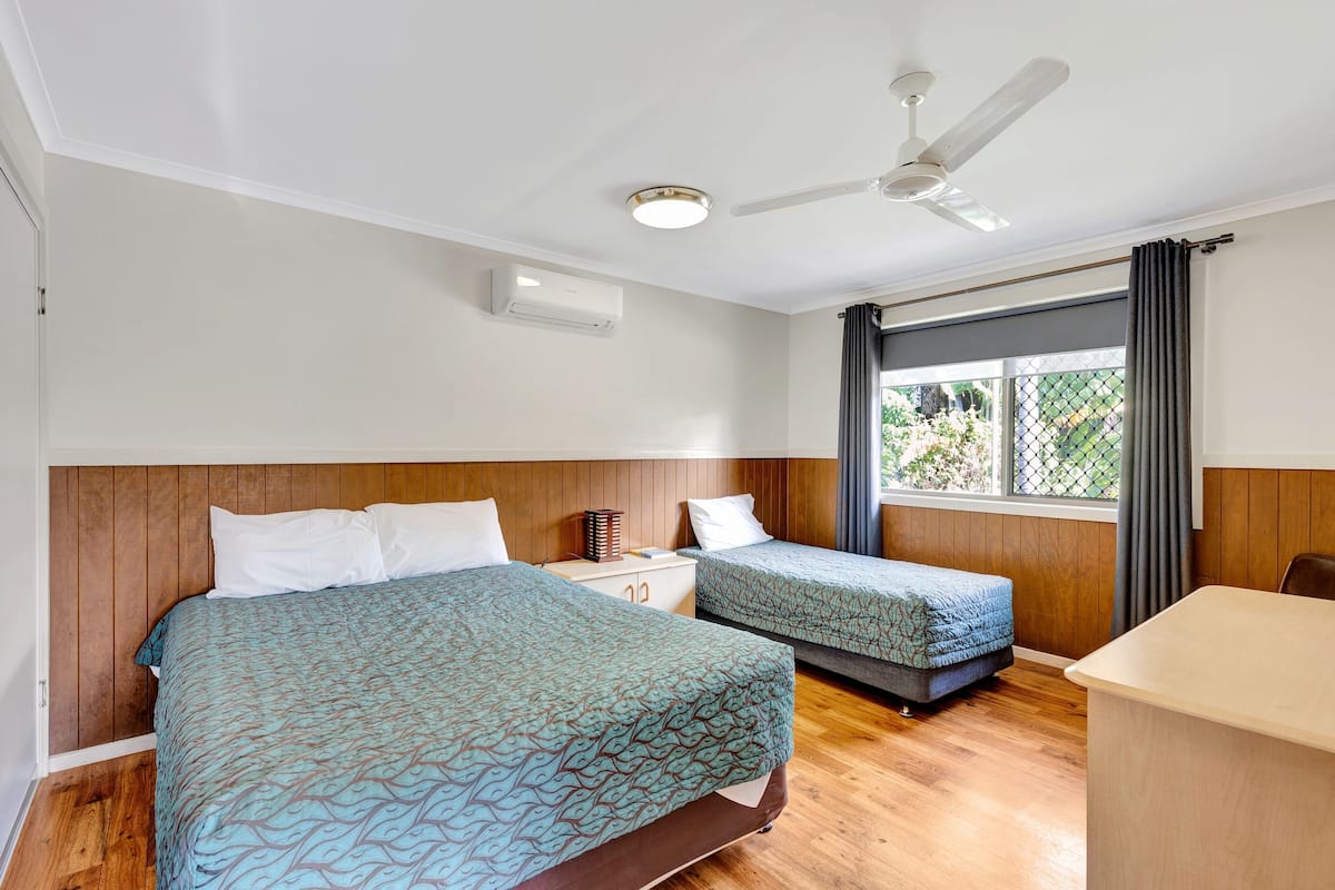 Habitación de hotel con dos camas, un escritorio, un ventilador de techo y una ventana con cortinas.