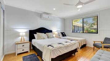 Un dormitorio con una cama grande, dos mesitas de noche, un ventilador de techo y una ventana con persianas.