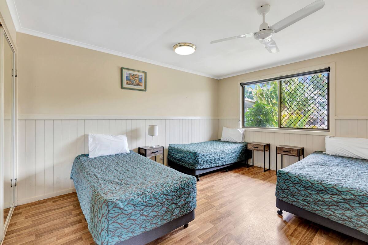 Una habitación con dos camas, ventilador de techo, ventana con vistas y un cuadro en la pared.