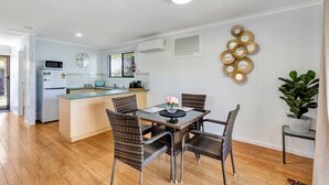 A modern kitchen with a central island, dining area with wicker chairs, and a decorative wall piece. - Sanctuary Lakes Fauna Retreat (Urangan)
